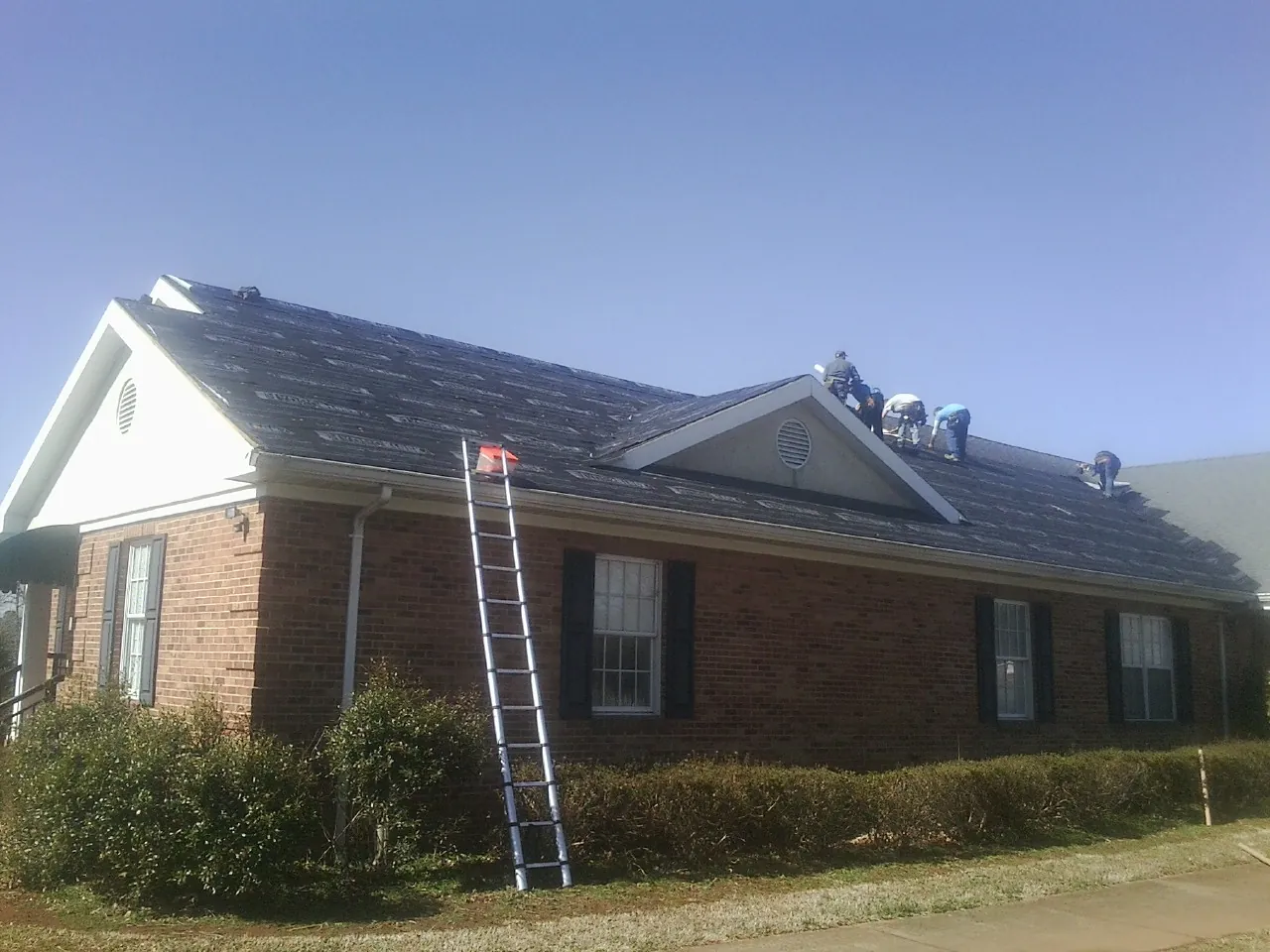 Crew tearing shingles off a brick ranch roof with a ladder set — Emergency Roof Repair work by our crew in Malvern