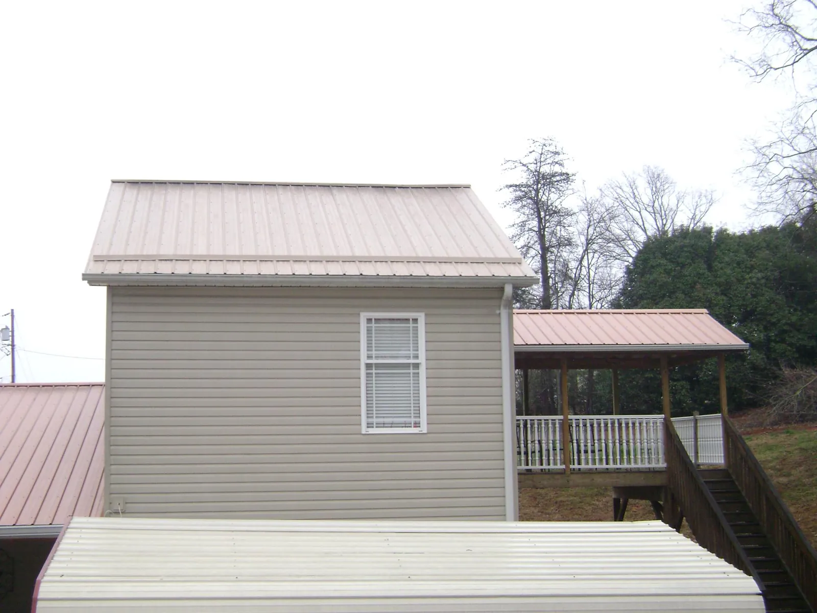 Tan metal roofs on a two story addition and attached porch, from a Roof Replacement job in Malvern